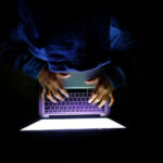 Hooded hacker Man with laptop stealing personal data from internet
